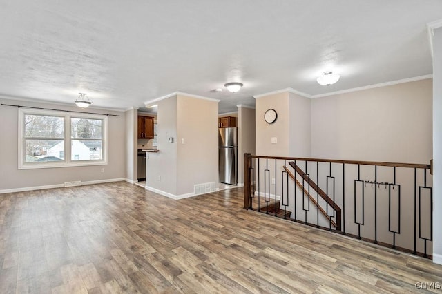 empty room featuring baseboards, crown molding, visible vents, and wood finished floors