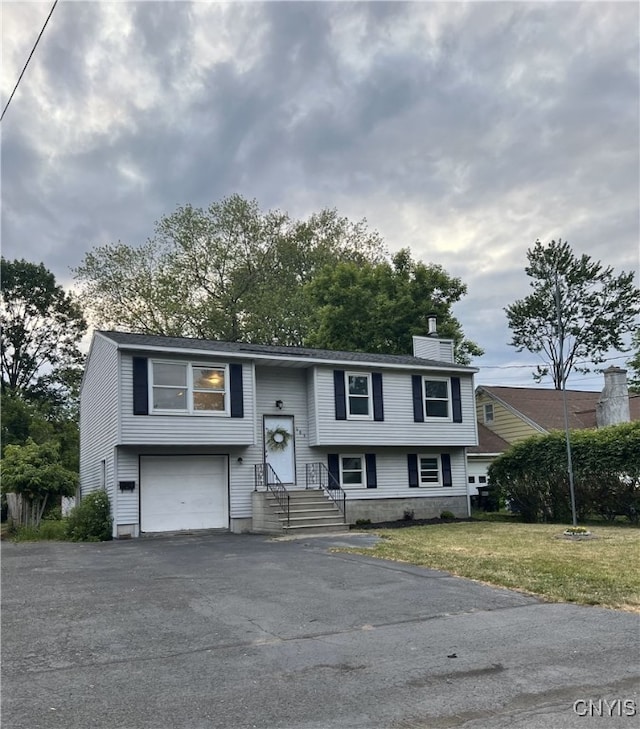 bi-level home featuring a garage, a front yard, driveway, and a chimney