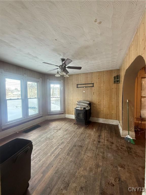 unfurnished living room with visible vents, baseboards, ceiling fan, dark wood-type flooring, and a wood stove