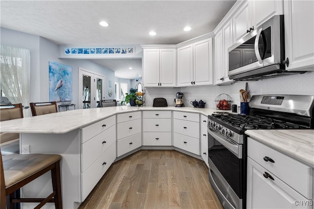 kitchen featuring french doors, stainless steel appliances, wood finished floors, a peninsula, and a kitchen bar