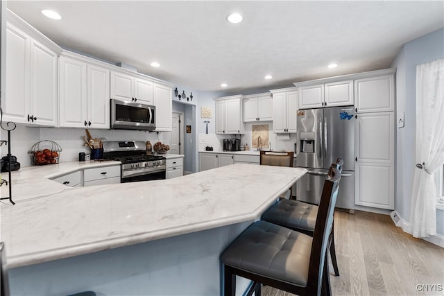 kitchen with a peninsula, white cabinetry, light wood-style floors, appliances with stainless steel finishes, and a kitchen bar