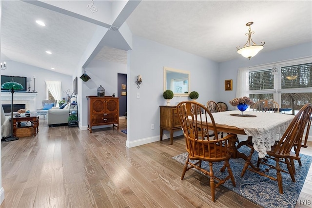 dining room featuring a fireplace, light wood finished floors, lofted ceiling, recessed lighting, and baseboards