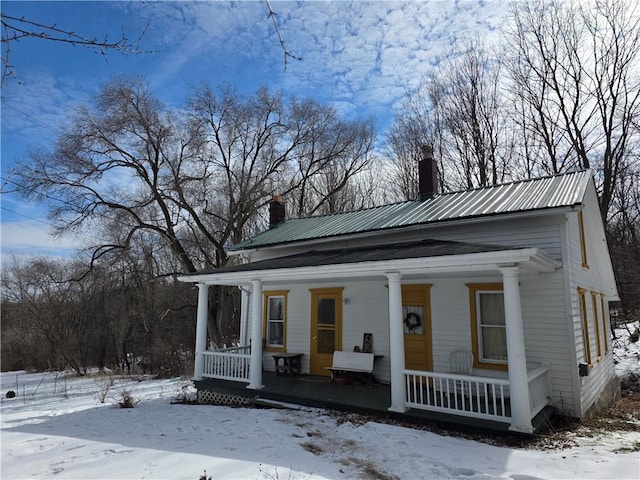 greek revival inspired property featuring covered porch, metal roof, and a chimney