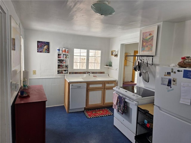 kitchen featuring white appliances, light countertops, a sink, and wainscoting