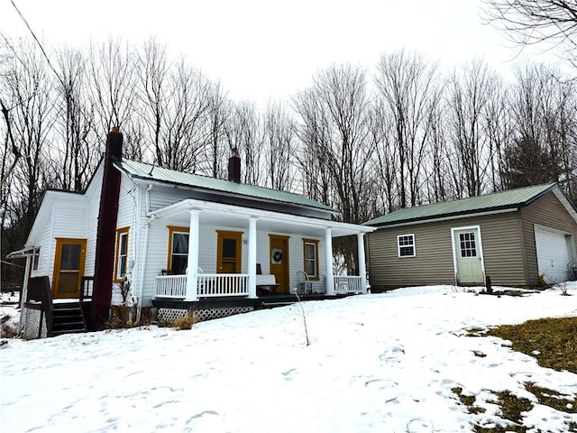 view of front of house featuring a chimney, covered porch, metal roof, a garage, and an outdoor structure