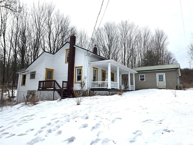 snow covered rear of property featuring covered porch and a chimney