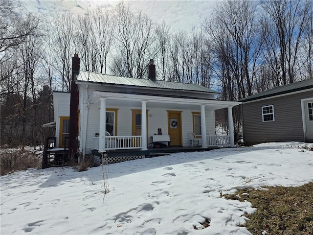 view of front facade with covered porch, metal roof, and a chimney