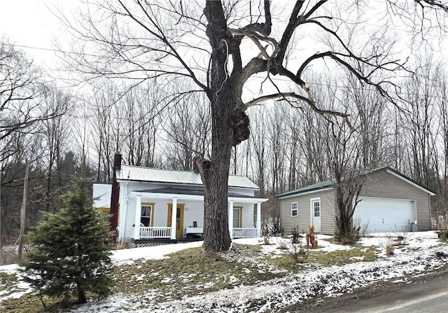 view of front facade with a garage, a chimney, metal roof, covered porch, and an outdoor structure