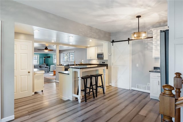 kitchen featuring a breakfast bar, dark countertops, stainless steel microwave, a barn door, and wood finished floors