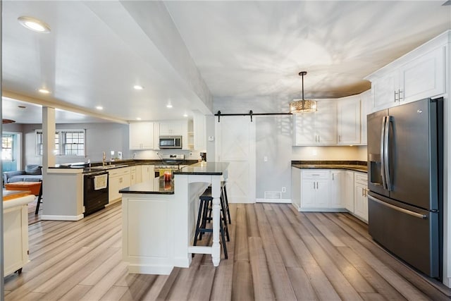 kitchen featuring light wood finished floors, appliances with stainless steel finishes, a barn door, and dark countertops