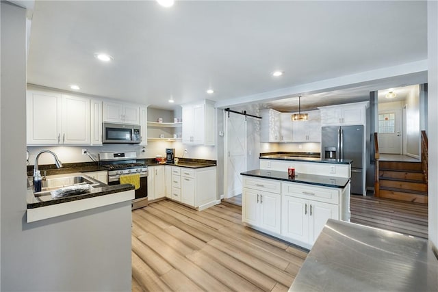 kitchen featuring a barn door, appliances with stainless steel finishes, light wood-type flooring, open shelves, and a sink