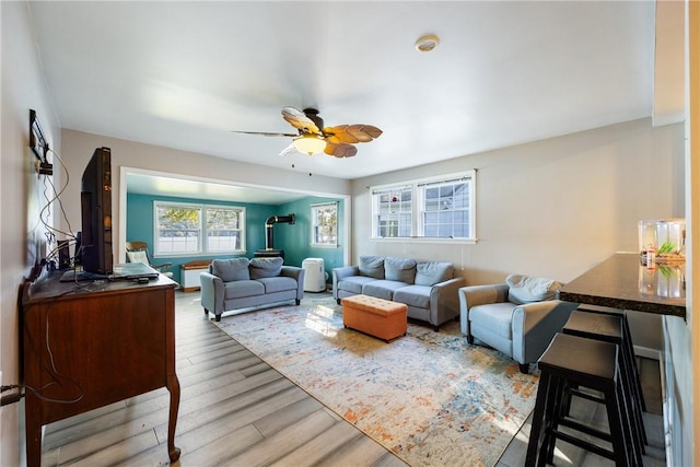 living area featuring a ceiling fan, a wood stove, and wood finished floors