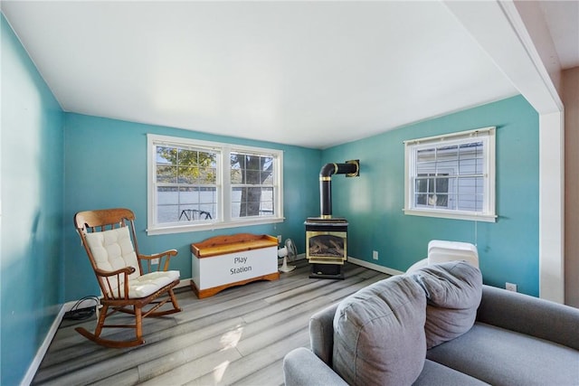 sitting room with a wood stove, baseboards, and wood finished floors