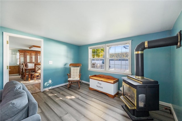 sitting room with wood finished floors, a wood stove, and baseboards