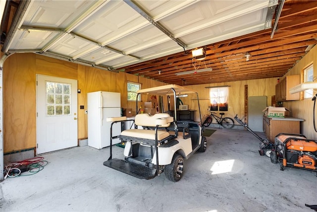 garage featuring a garage door opener, freestanding refrigerator, and wood walls