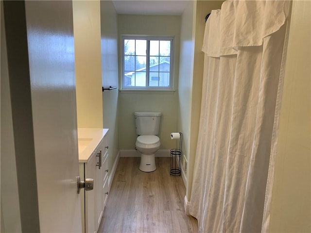 bathroom featuring a shower with shower curtain, toilet, vanity, wood finished floors, and baseboards