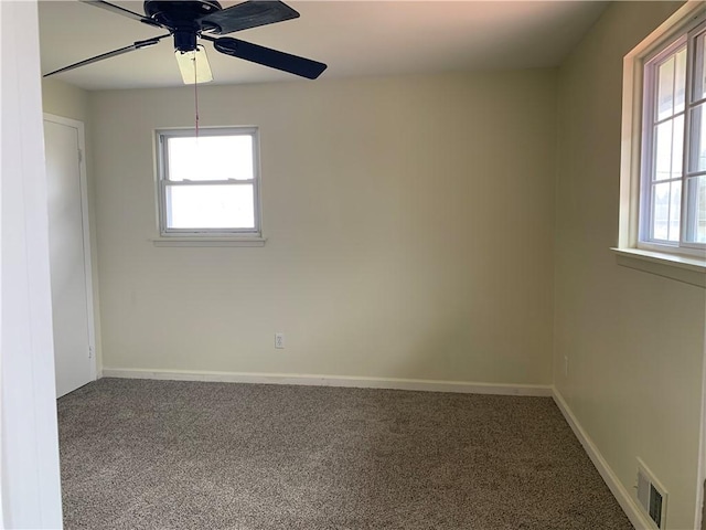 carpeted spare room with a healthy amount of sunlight, ceiling fan, visible vents, and baseboards