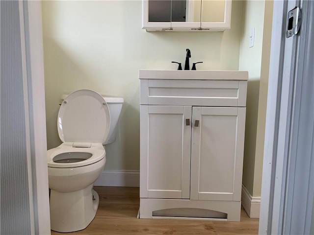 bathroom with toilet, wood finished floors, vanity, and baseboards