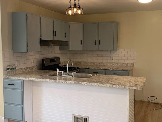 kitchen featuring a peninsula, stainless steel gas range, light countertops, under cabinet range hood, and a sink