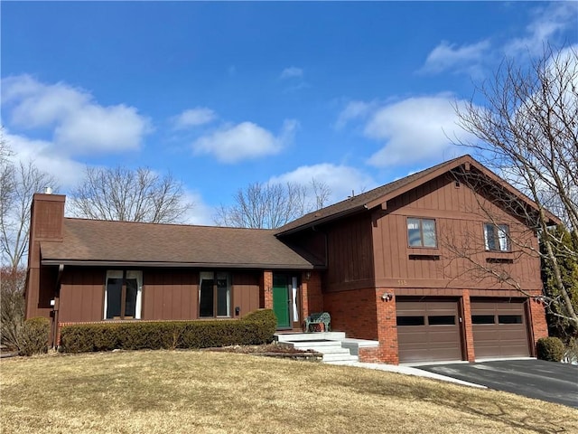 split level home with brick siding, a chimney, an attached garage, driveway, and a front lawn