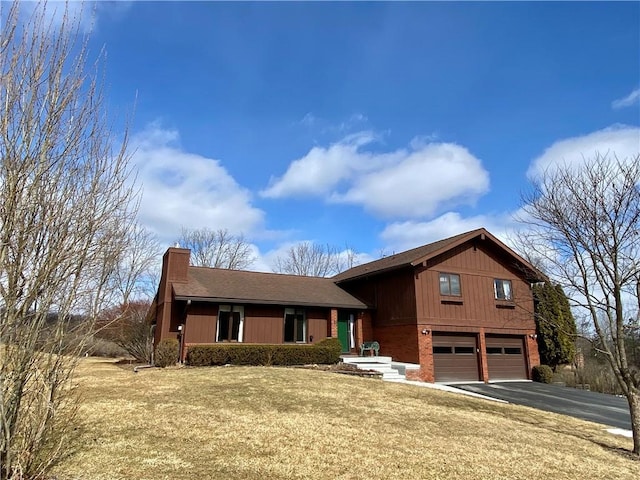 view of front of property with aphalt driveway, a garage, brick siding, a front lawn, and a chimney