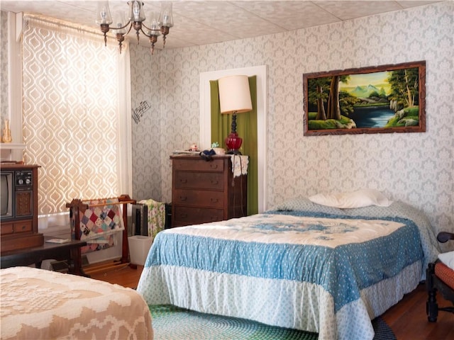 bedroom featuring wallpapered walls, wood finished floors, and an inviting chandelier