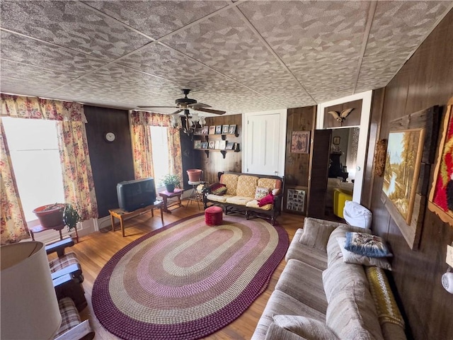 living room with ceiling fan, wood walls, and wood finished floors