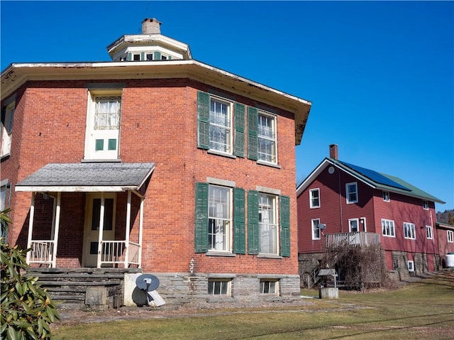 view of home's exterior with covered porch, a yard, a chimney, and brick siding