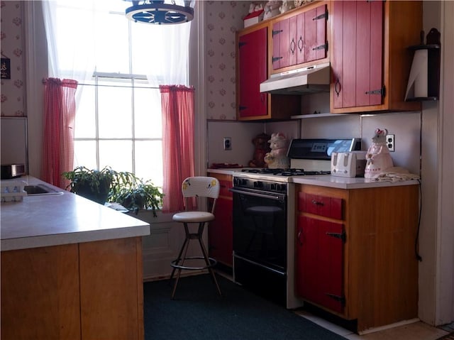 kitchen featuring light countertops, wallpapered walls, under cabinet range hood, and gas range oven