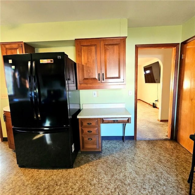 kitchen with brown cabinetry, freestanding refrigerator, light countertops, and baseboards