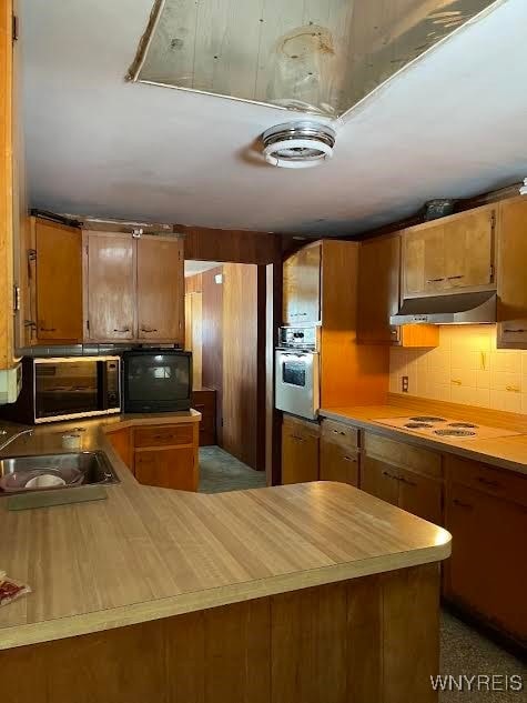 kitchen featuring brown cabinets, light countertops, ventilation hood, stainless steel oven, and a sink