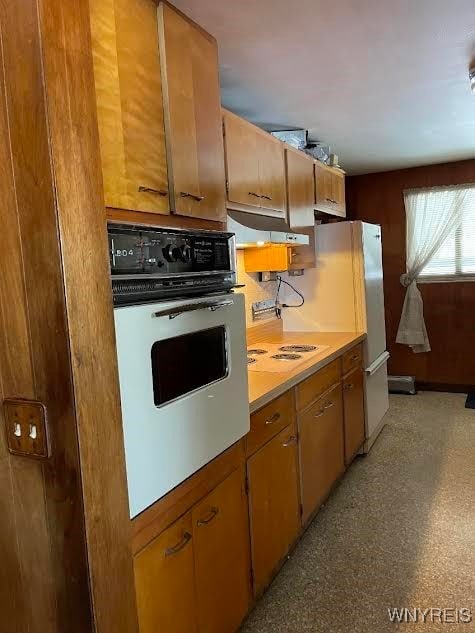 kitchen featuring brown cabinetry, white appliances, light countertops, and under cabinet range hood