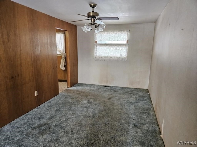 empty room with carpet, wooden walls, and ceiling fan