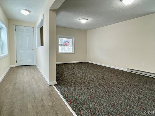 interior space featuring baseboard heating, a textured ceiling, baseboards, and wood finished floors