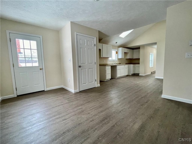 unfurnished living room featuring lofted ceiling, dark wood-style flooring, a textured ceiling, and baseboards