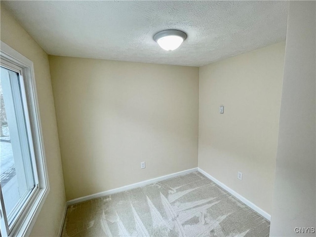 spare room featuring baseboards, a textured ceiling, and light colored carpet