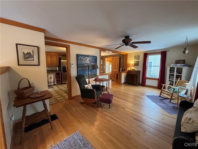 living area with light wood-style floors, crown molding, baseboards, and a ceiling fan