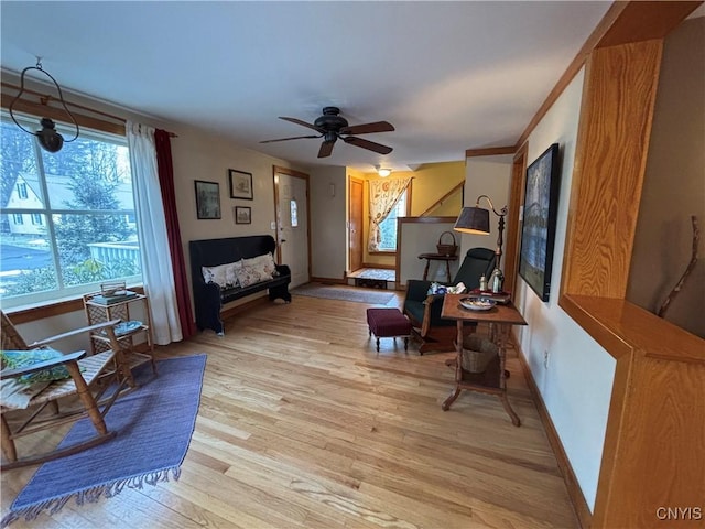 living room featuring baseboards, ceiling fan, and light wood finished floors