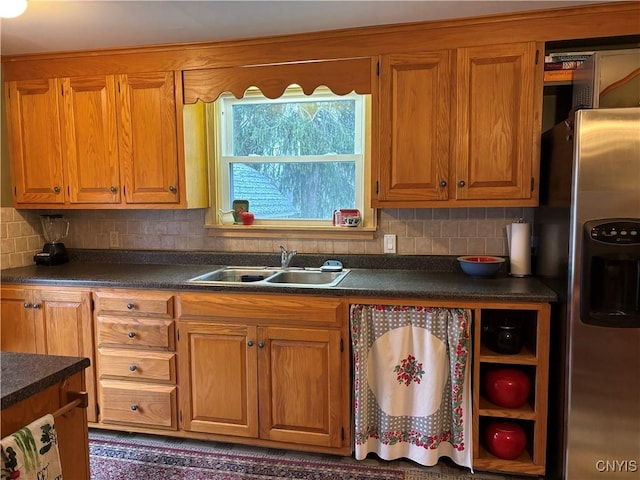 kitchen with dark countertops, backsplash, a sink, and stainless steel refrigerator with ice dispenser