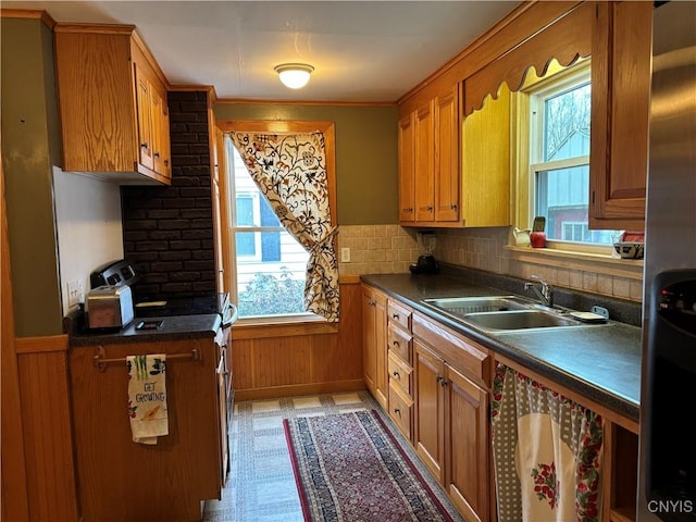 kitchen featuring wainscoting, dark countertops, brown cabinets, light floors, and a sink