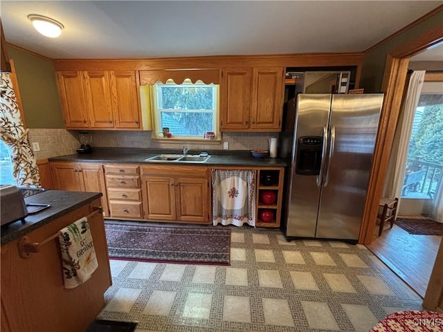 kitchen with dark countertops, tasteful backsplash, stainless steel refrigerator with ice dispenser, and a sink