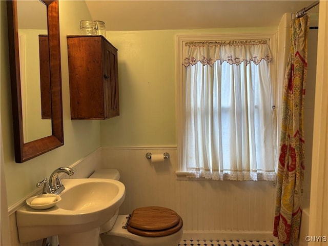 bathroom featuring a shower with shower curtain, a wainscoted wall, a sink, and toilet