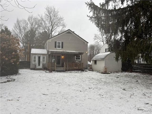 snow covered back of property with an outbuilding, a storage unit, fence, and a deck