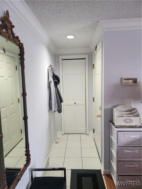 hall featuring a textured ceiling, ornamental molding, light tile patterned floors, and baseboards