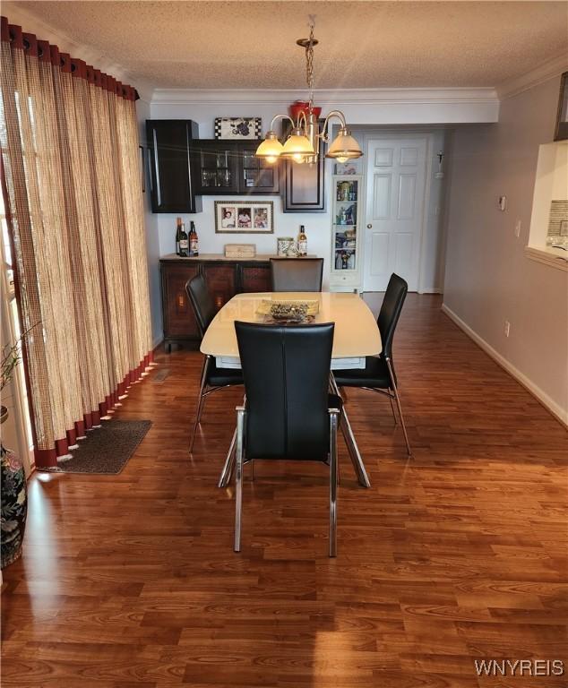 dining space featuring a textured ceiling, dark wood-style flooring, a notable chandelier, and crown molding