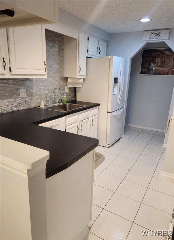 kitchen featuring white refrigerator with ice dispenser, dark countertops, a sink, a textured ceiling, and backsplash