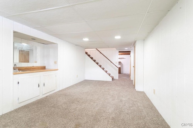 finished below grade area featuring stairway, a drop ceiling, a sink, and light colored carpet