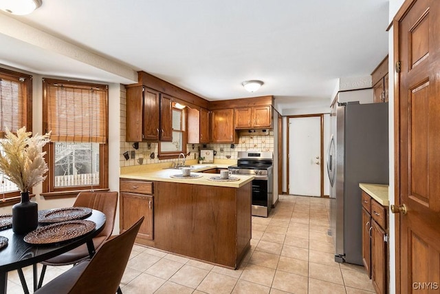 kitchen with a peninsula, a sink, light countertops, appliances with stainless steel finishes, and backsplash