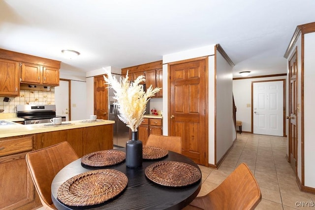 kitchen with light tile patterned floors, tasteful backsplash, electric range, brown cabinets, and light countertops