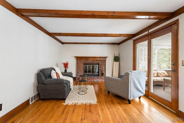 living area featuring visible vents, a brick fireplace, wood finished floors, beamed ceiling, and baseboards